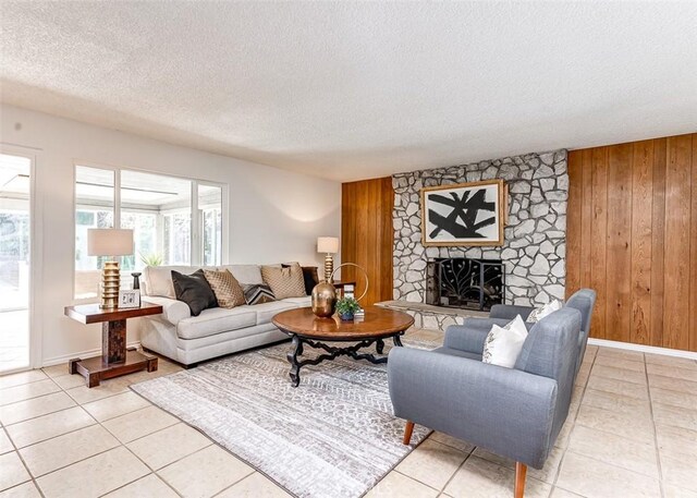 living room with wooden walls, a textured ceiling, a stone fireplace, and light tile patterned floors