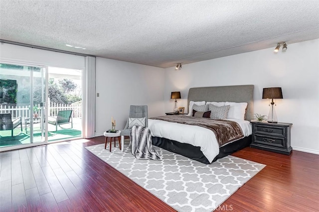 bedroom with a textured ceiling, access to outside, dark wood-type flooring, and baseboards