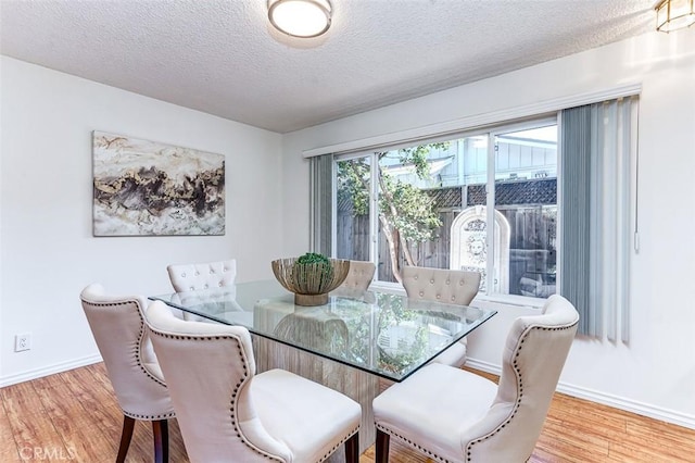 dining space featuring a textured ceiling, light wood finished floors, and baseboards