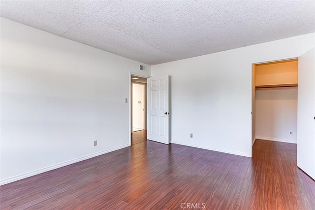 unfurnished bedroom featuring a textured ceiling, baseboards, visible vents, and wood finished floors