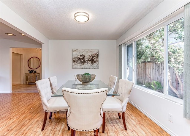 dining space with light wood-type flooring, baseboards, and a textured ceiling