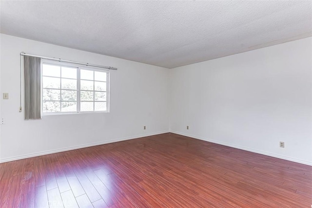 spare room featuring a textured ceiling, dark wood-style flooring, and baseboards