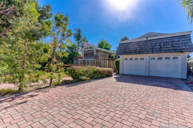 view of front of property with mansard roof, a garage, an outdoor structure, fence, and decorative driveway