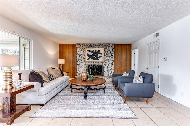 living room featuring an accent wall, a stone fireplace, visible vents, and wooden walls