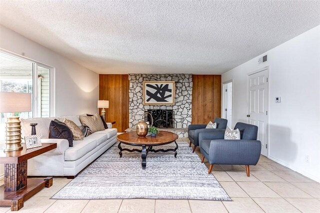 living area featuring wooden walls, a fireplace, visible vents, and a textured ceiling