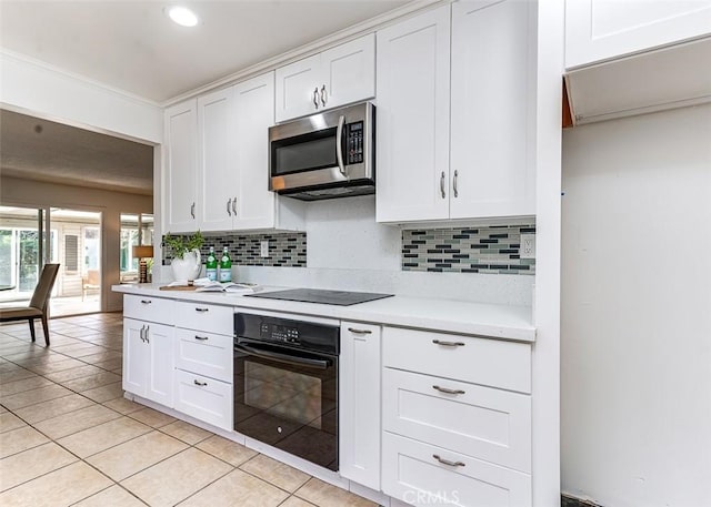 kitchen featuring light tile patterned floors, light countertops, black appliances, white cabinetry, and backsplash