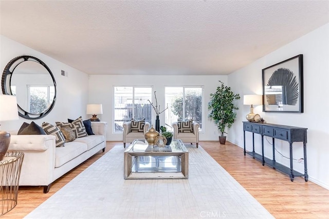 living area with light wood-style floors, baseboards, visible vents, and a textured ceiling