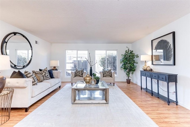 living area featuring baseboards, light wood finished floors, visible vents, and a textured ceiling