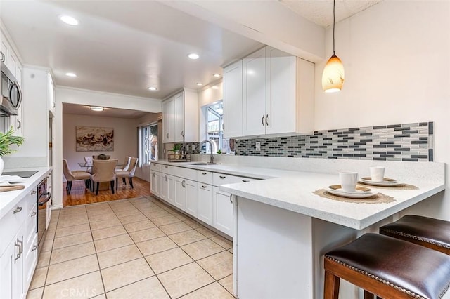 kitchen featuring light tile patterned floors, a sink, backsplash, white cabinetry, and decorative light fixtures
