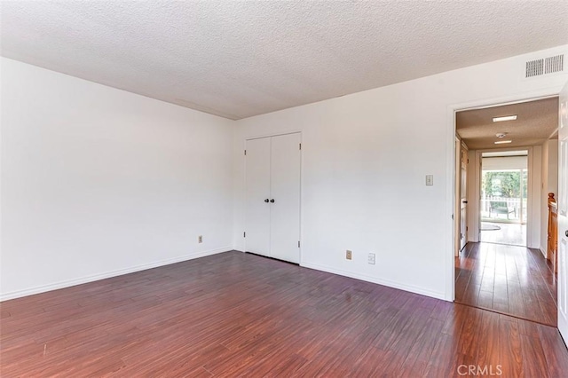 spare room featuring visible vents, dark wood finished floors, a textured ceiling, and baseboards