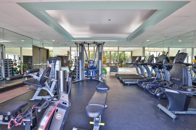 workout area with a paneled ceiling, floor to ceiling windows, and a raised ceiling