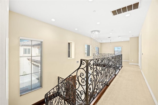 hallway with plenty of natural light, light carpet, and a notable chandelier