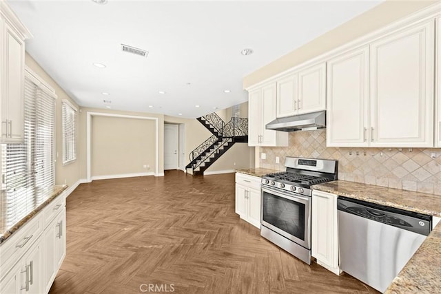 kitchen featuring appliances with stainless steel finishes, parquet floors, white cabinets, decorative backsplash, and light stone countertops