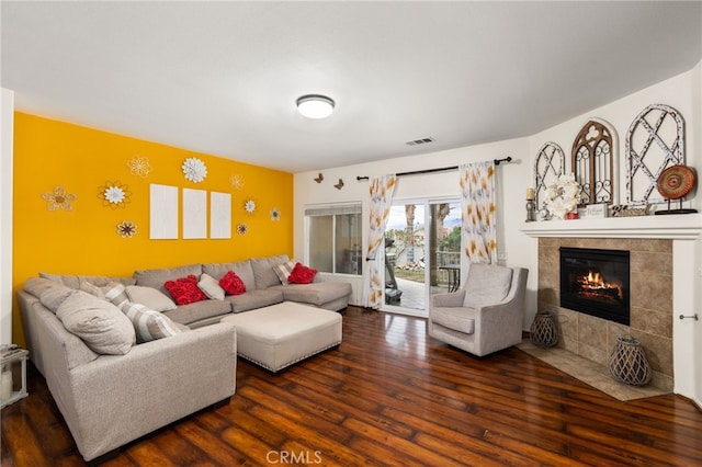 living room with a tile fireplace and dark wood-type flooring