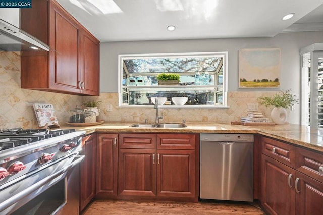 kitchen featuring sink, decorative backsplash, light stone counters, stainless steel appliances, and wall chimney range hood