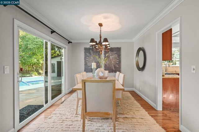 dining area with an inviting chandelier, ornamental molding, sink, and light hardwood / wood-style flooring