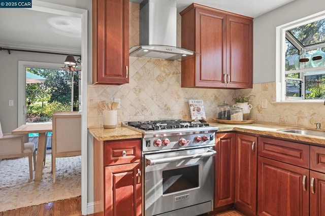 kitchen featuring premium range, sink, backsplash, light stone counters, and wall chimney range hood