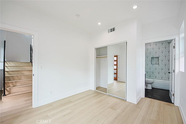 unfurnished bedroom with ensuite bath, a closet, and light hardwood / wood-style flooring