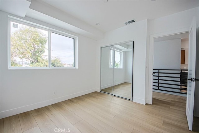 unfurnished bedroom featuring multiple windows, light hardwood / wood-style flooring, and a closet