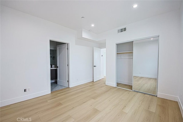 unfurnished bedroom with ensuite bath, a closet, and light wood-type flooring