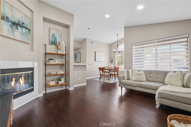 living room with vaulted ceiling, dark wood-type flooring, a notable chandelier, and a fireplace