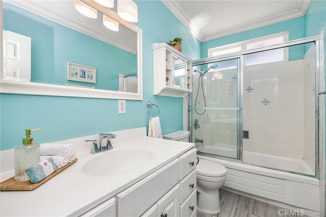 full bathroom featuring bath / shower combo with glass door, hardwood / wood-style floors, ornamental molding, vanity, and toilet