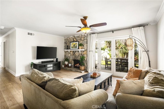 living room featuring crown molding, light hardwood / wood-style flooring, ceiling fan, a stone fireplace, and french doors