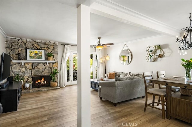 living room featuring hardwood / wood-style flooring, ornamental molding, a stone fireplace, and ceiling fan with notable chandelier