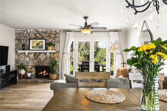 living room featuring a stone fireplace, ornamental molding, french doors, and light wood-type flooring