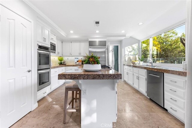 kitchen featuring white cabinetry, a kitchen island, built in appliances, and a kitchen bar