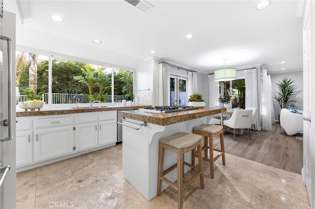 kitchen with a kitchen bar, stainless steel gas cooktop, decorative light fixtures, a kitchen island, and white cabinets