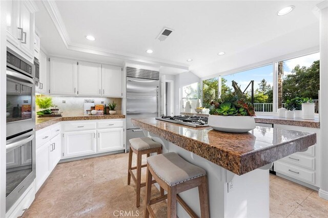 kitchen with a kitchen island, a breakfast bar, white cabinets, backsplash, and stainless steel appliances