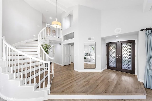 entrance foyer with wood-type flooring, a towering ceiling, and french doors