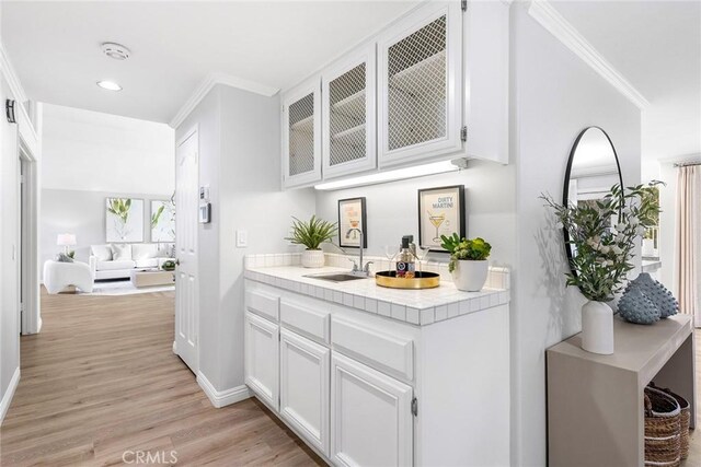 bar featuring sink, crown molding, white cabinetry, light hardwood / wood-style floors, and tile countertops