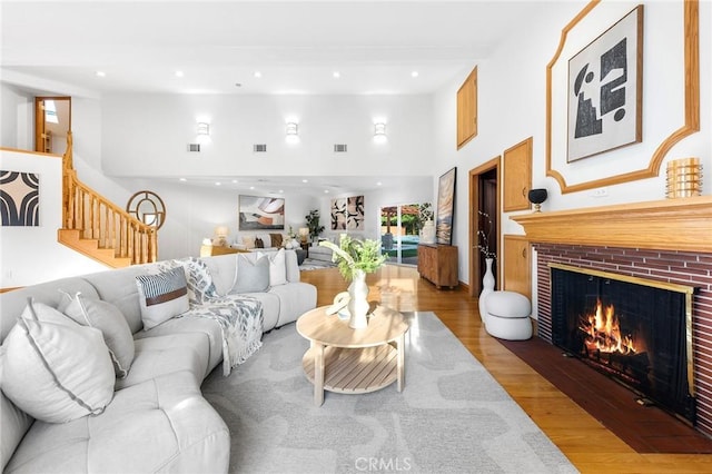 living room featuring a towering ceiling, hardwood / wood-style floors, and a brick fireplace