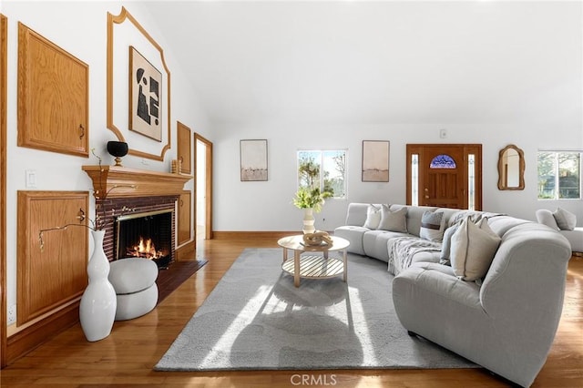 living room with vaulted ceiling, light hardwood / wood-style floors, and a brick fireplace