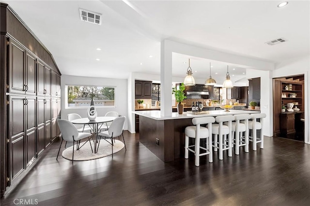 kitchen featuring pendant lighting, a breakfast bar area, dark brown cabinets, a center island, and dark hardwood / wood-style flooring