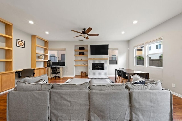 living room featuring a tile fireplace, built in desk, ceiling fan, and dark hardwood / wood-style flooring