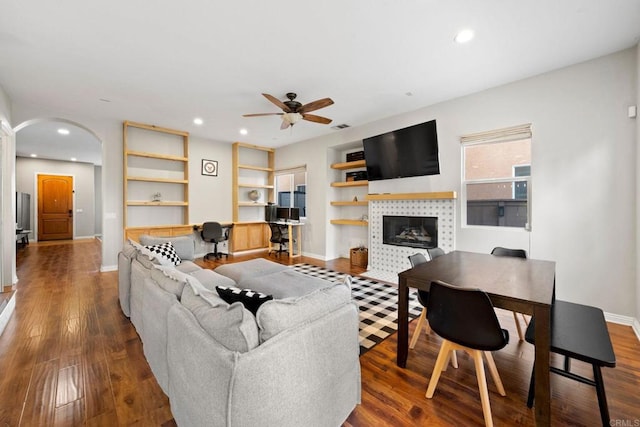 living room featuring ceiling fan, a tiled fireplace, hardwood / wood-style floors, and built in desk