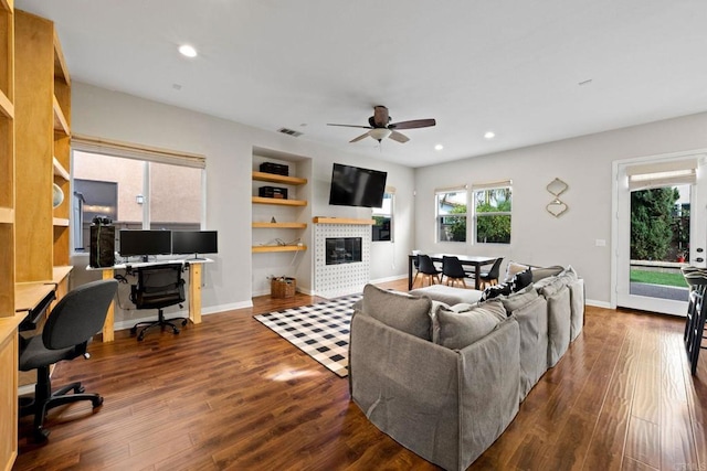 living room featuring ceiling fan, dark hardwood / wood-style floors, built in features, and a fireplace