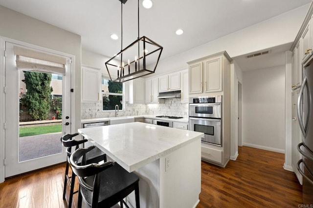 kitchen with sink, a center island, hanging light fixtures, appliances with stainless steel finishes, and dark hardwood / wood-style flooring