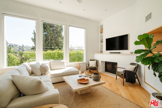 living room with a fireplace, light hardwood / wood-style flooring, built in features, and ceiling fan