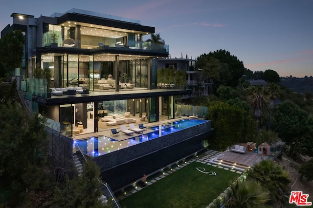 back house at dusk with outdoor lounge area, a pool with hot tub, and a patio area