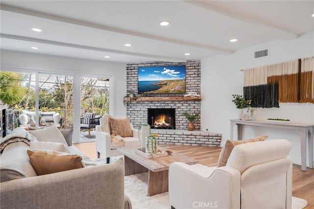 living room with beamed ceiling, light hardwood / wood-style floors, and a brick fireplace