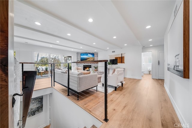 living room featuring a brick fireplace, beam ceiling, and light hardwood / wood-style flooring