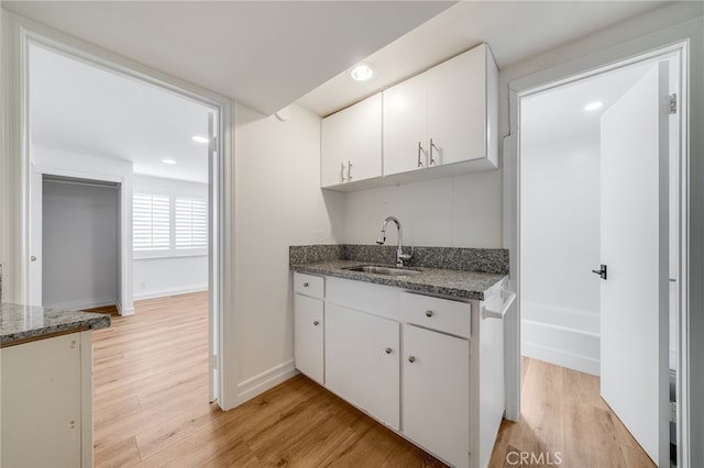 kitchen with white cabinetry, sink, light hardwood / wood-style floors, and dark stone countertops