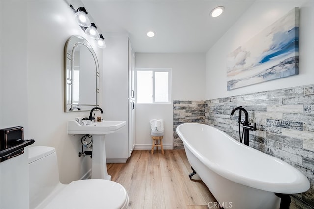 bathroom with tile walls, hardwood / wood-style floors, a bathtub, and toilet