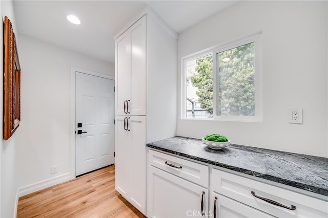 kitchen featuring white cabinetry, light hardwood / wood-style flooring, and dark stone countertops