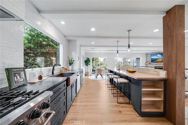 kitchen with decorative light fixtures, butcher block counters, backsplash, light hardwood / wood-style floors, and gas stove