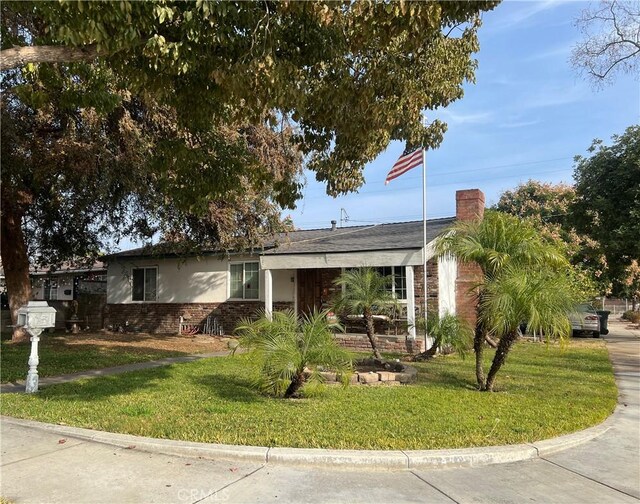 single story home featuring brick siding, a front lawn, a chimney, and stucco siding